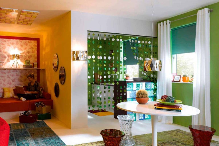 Pohled do světlého obývacího pokoje s různými obytnými prostory, jako je posezení, jídelní kout a kuchyň.