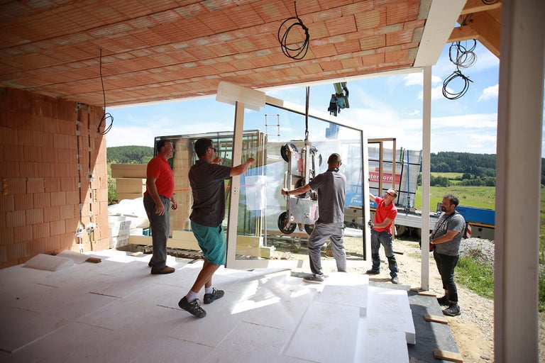 Montáž velkého okenního prvku jeřábem na staveništi.