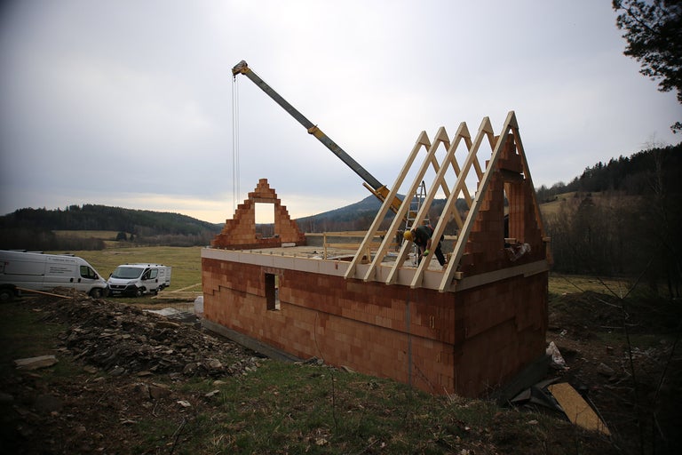 Staveniště domu s cihlovou zdí a dřevěnou konstrukcí střechy