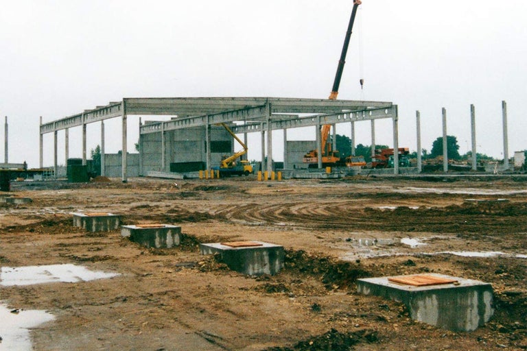 Stavba skladové haly s betonovými pilíři a jeřáby na staveništi