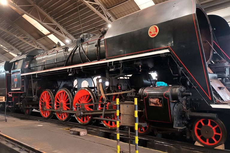 Černá parní lokomotiva s červenými koly stojí v hale.