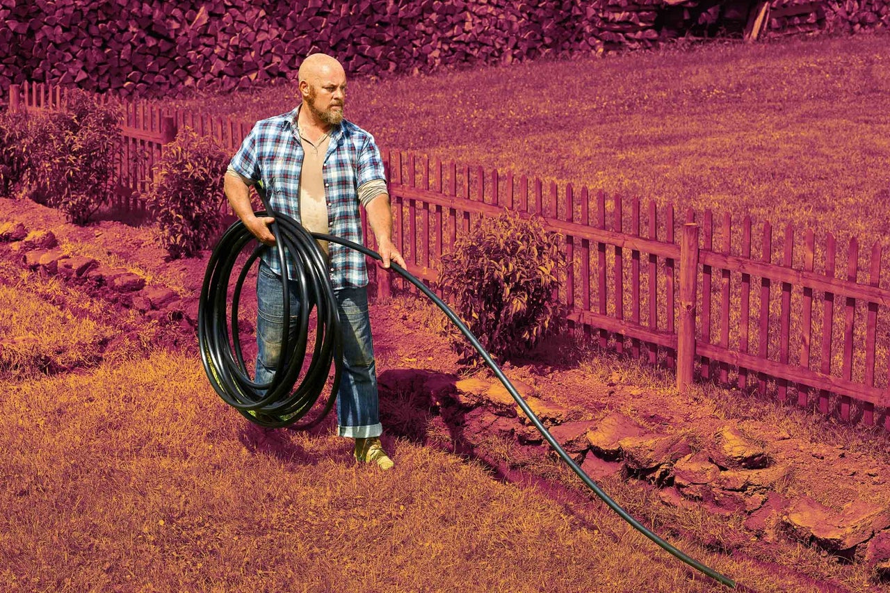 Muž nese roli černé polyethylenové trubky pro zavlažování v zahradě s dřevěným plotem.