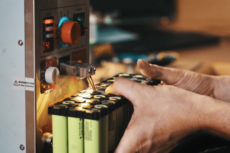 Osoba svařuje baterie se svářečkou.