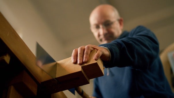 Muž řeže dřevo ruční pilou v pokosnici