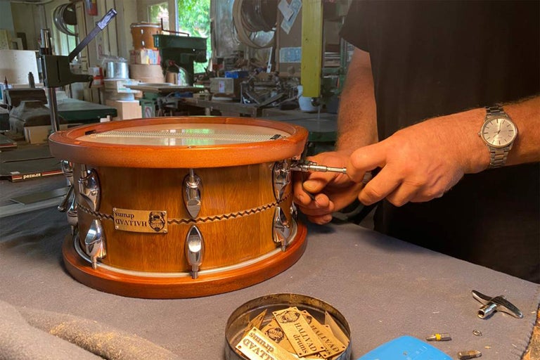 Muž ladí dřevěný buben s chromovaným kováním a logem Hallvad Drums.