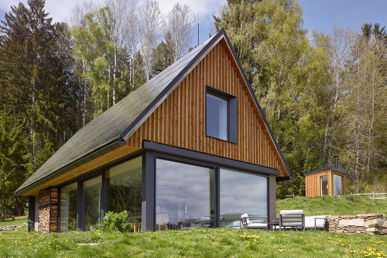 Moderní dřevěný dům se solárními panely na střeše a velkými okny ve venkovském prostředí