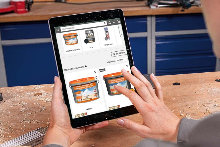 Osoba používá tablet k prohlížení internetového obchodu Hornbach a výběru barev v prostředí dílny.