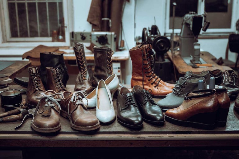 Kolekce obuvi na stole se šicími stroji v pozadí