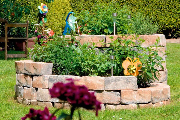 Zvýšený záhon z kamene s bylinkami a dekorací na zahradě