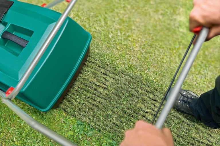 Osoba používá provzdušňovač trávníku na travnaté ploše.