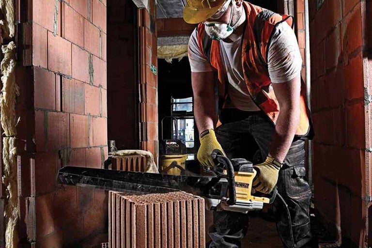 Stavební dělník s ochrannými pomůckami řeže cihlu pilou na kámen.