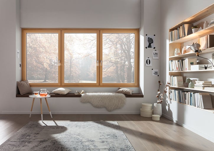 Světlý obývací pokoj s dřevěnými okny, knihovnou a kobercem