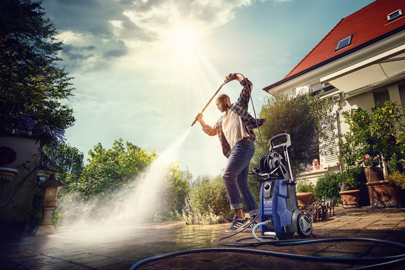 Muž čistí terasu vysokotlakým čističem venku.