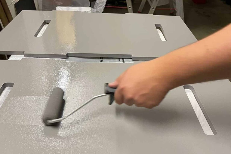 Osoba natírá desku malířským válečkem.