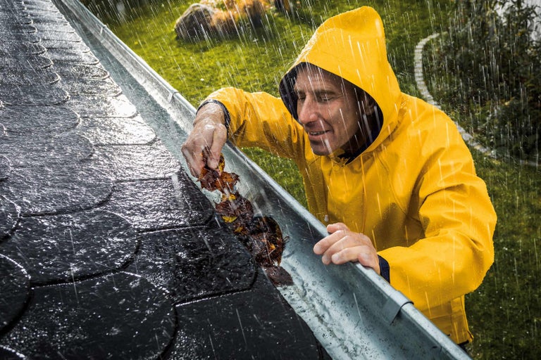 Muž v dešti čistí okap od listí.