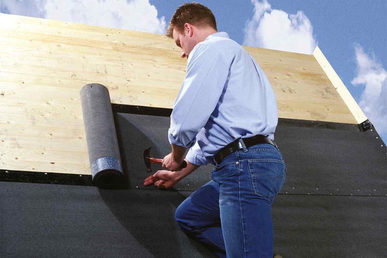 Řemeslník připevňuje lepenku na střechu kladivem.