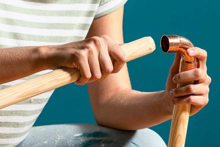 Osoba spojuje měděnou trubku s dřevěnou tyčí.