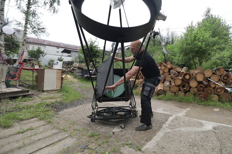 Muž sestavuje velký astronomický teleskop venku.