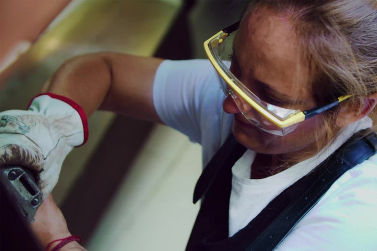 Žena s ochrannými brýlemi a pracovními rukavicemi při práci.