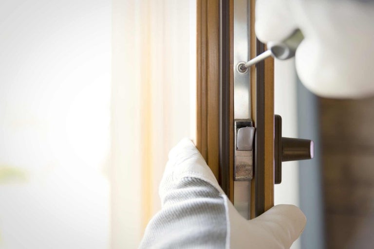 Osoba upevňuje zámek ke dveřím pomocí šroubováku.