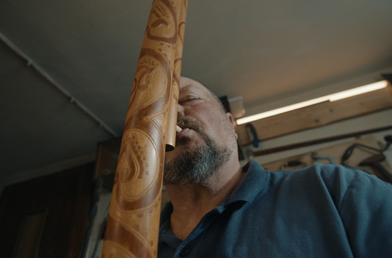 Muž hraje na zdobené didgeridoo.
