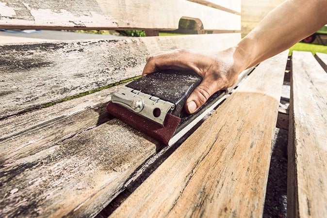 Ruka brousí dřevěnou lavici brusným blokem.