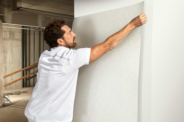 Muž upevňuje sklolaminátovou netkanou textilii na zeď, příprava na malování
