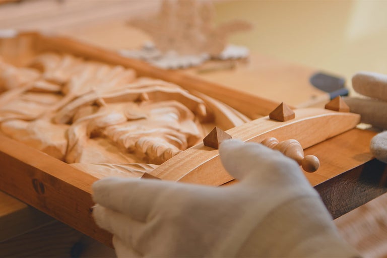 Dřevěný reliéf s vyřezávanou postavou a dřevěným rámem, držený rukama v rukavicích