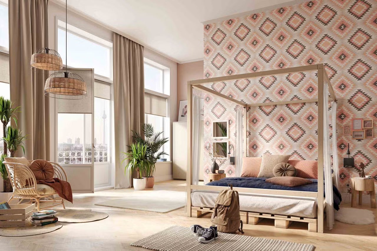 Světlá ložnice s postelí s nebesy z paletového dřeva, geometrickou tapetou, ratanovým křeslem, pletenými lampami a velkými okny.