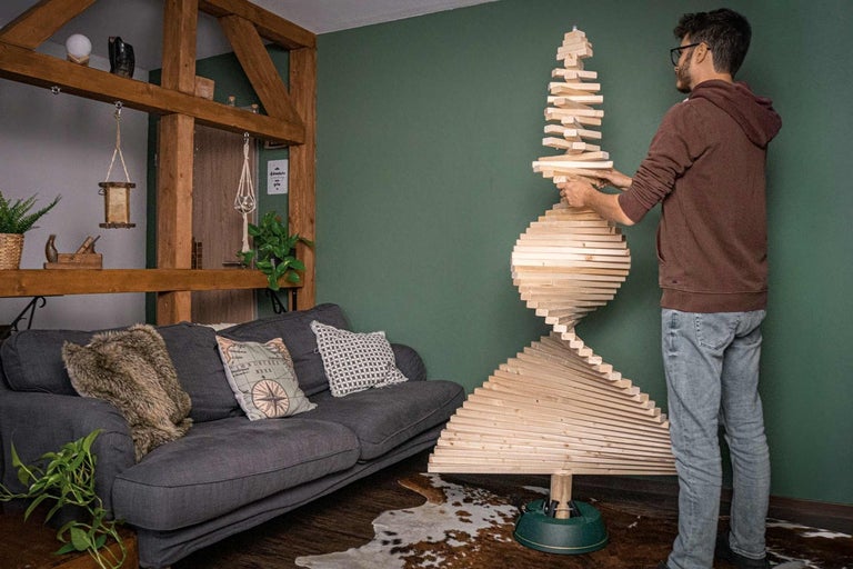 Muž sestavuje spirálovitý vánoční strom z dřevěných lamel v obývacím pokoji