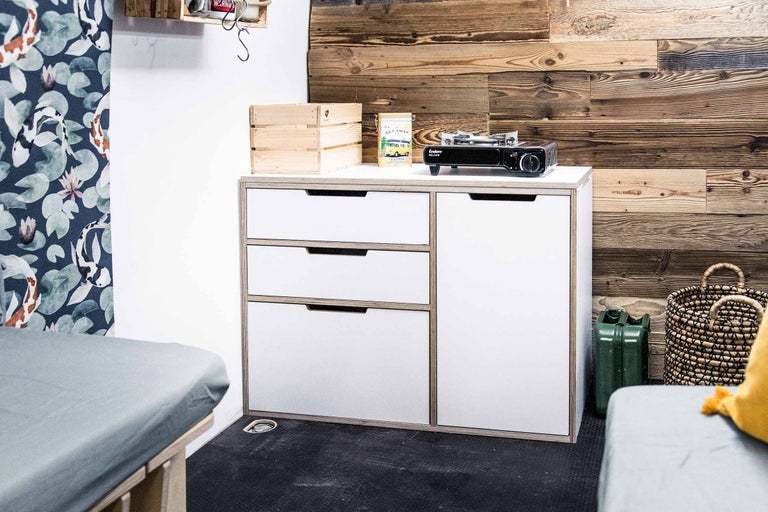 Scéna s komodou, dřevěnou bednou a plynovým vařičem