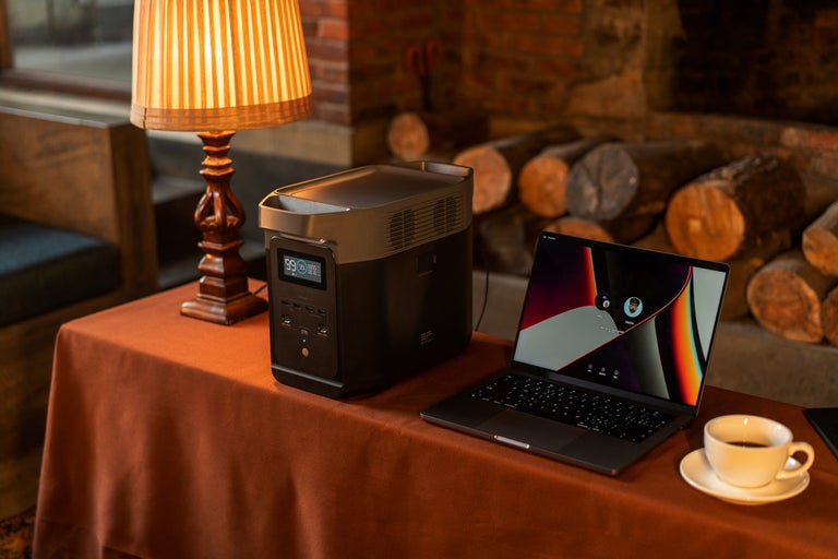 Přenosná napájecí stanice vedle notebooku a šálku kávy na stole