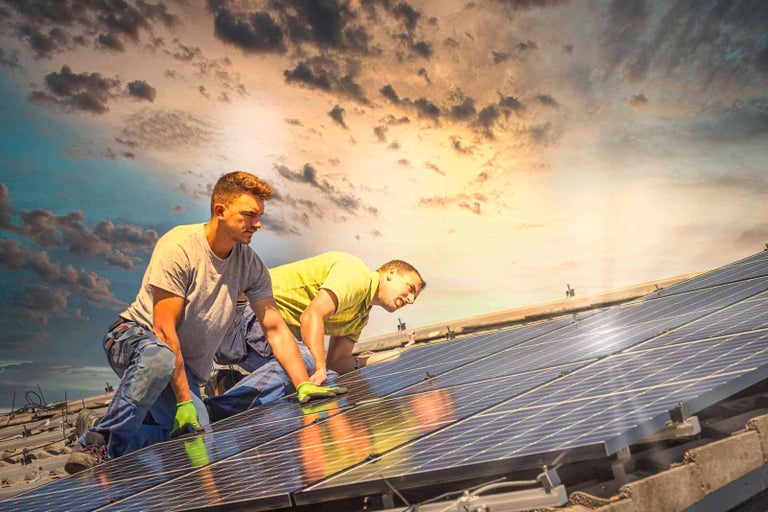 Dva pracovníci instalují solární panely na střechu