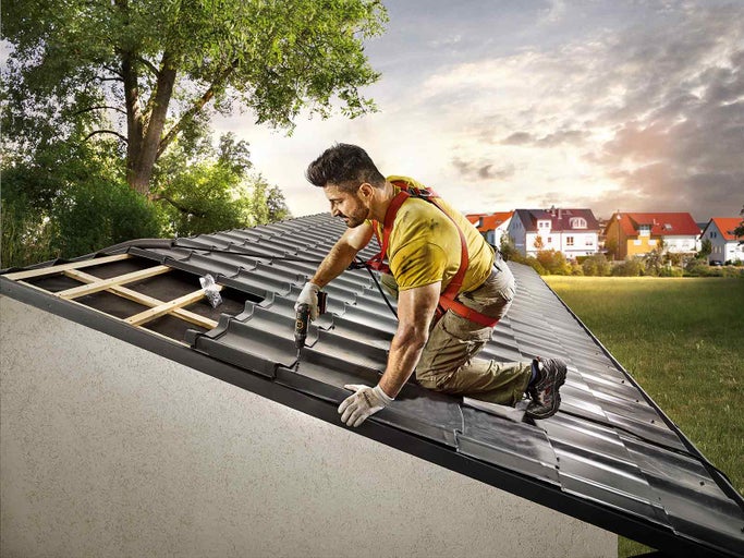 Pokrývač připevňuje střešní tašky aku šroubovákem na střechu.