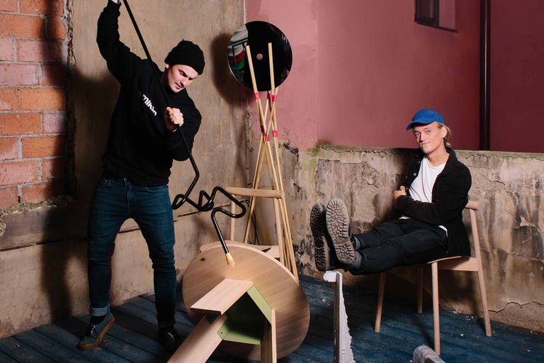 Scéna se dvěma lidmi, lampou a nábytkem v místnosti s neomítnutými stěnami