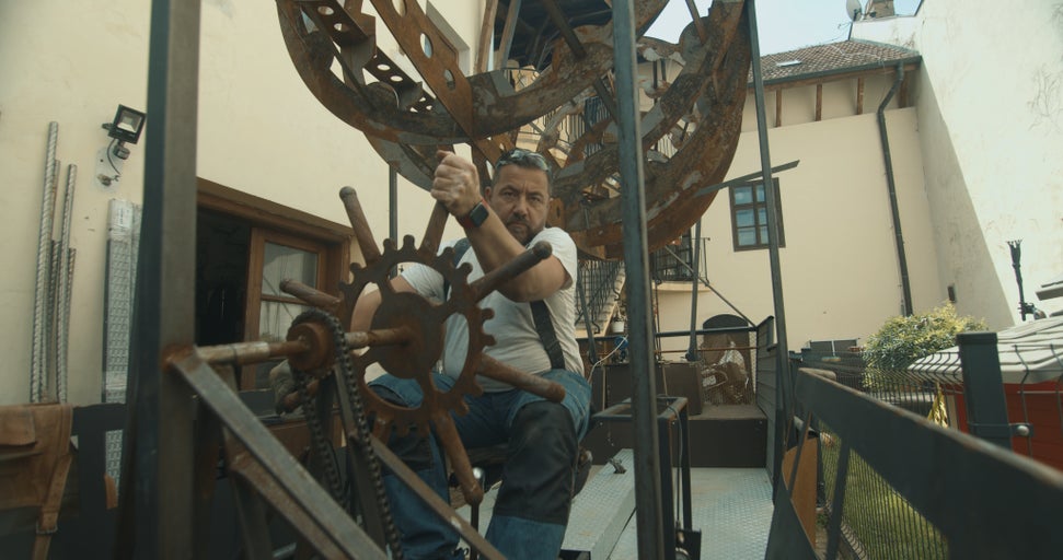 Muž obsluhuje velkou kovovou konstrukci s ozubeným kolem a řetězem venku