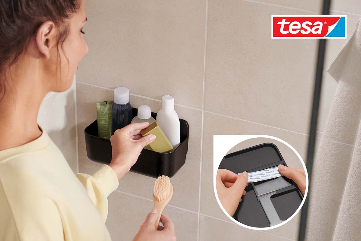 Žena plní černou sprchovou polici koupelnovými potřebami v koupelně, logo Tesa