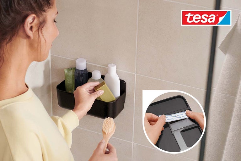 Žena plní černou sprchovou polici koupelnovými potřebami v koupelně, logo Tesa