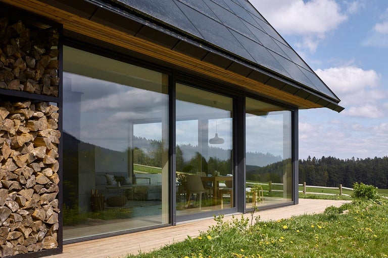 Moderní dům se skleněnou fasádou, hromadou dřeva a solární střechou