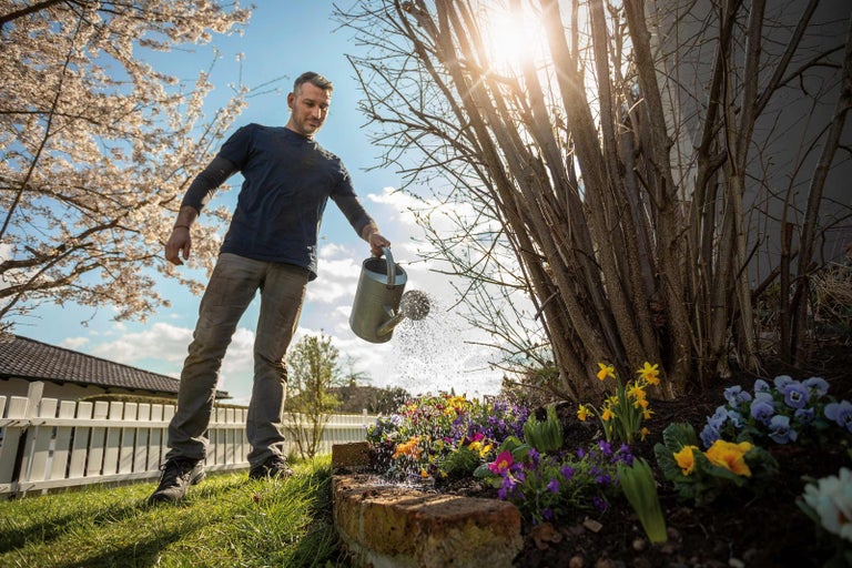 Muž zalévá květiny konví na zahradě.