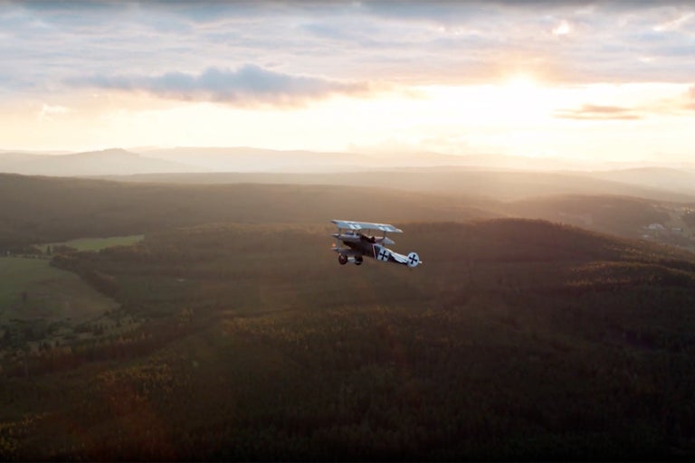 Dvouplošník letící nad lesní krajinou