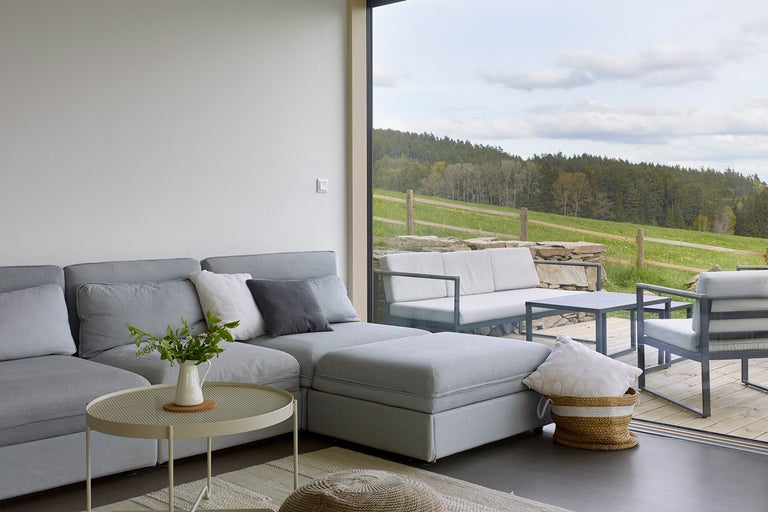 Světlý obývací pokoj s šedou pohovkou, odkládacím stolkem a výhledem do zeleně.