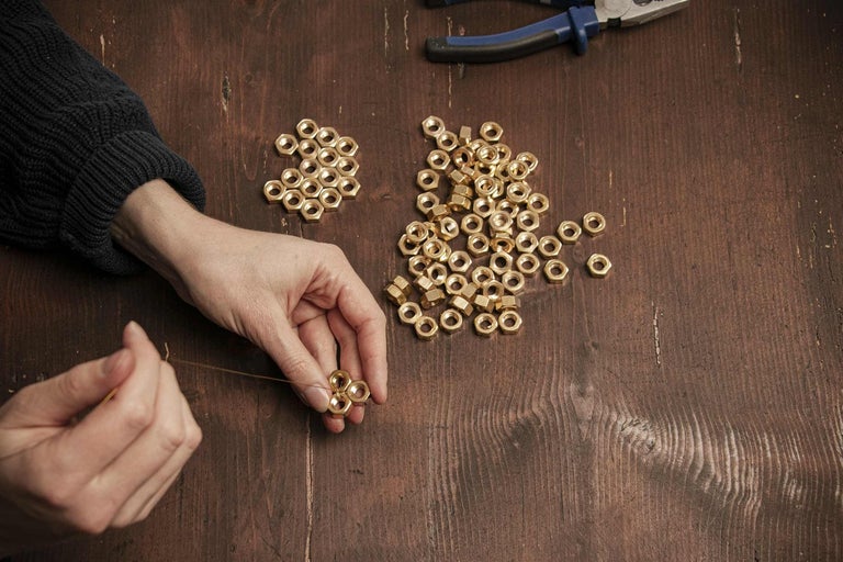 Osoba navléká mosazné matice na nit na dřevěném stole.