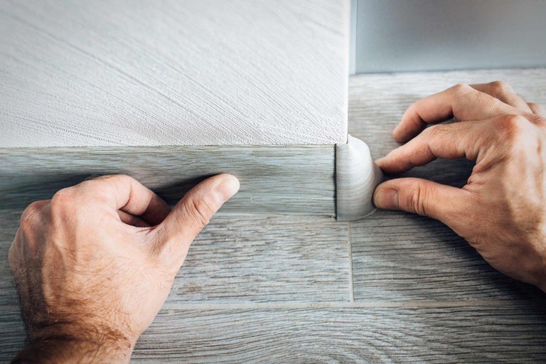 Ruce montují podlahovou lištu na zeď na dřevěné podlaze