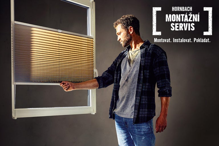 Muž ovládá okenní plisovanou žaluzii. V pozadí montážní servis Hornbach.