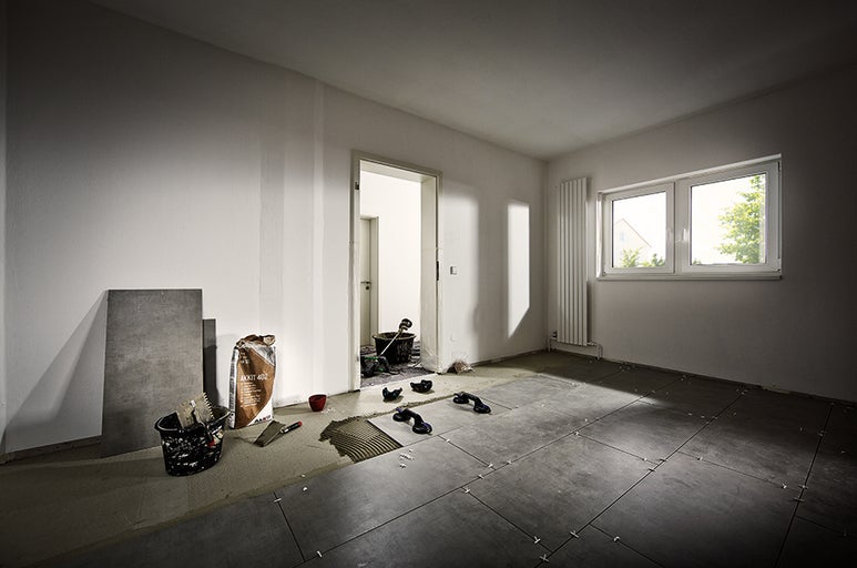 Pokládka dlažby v místnosti s dlaždicemi, nářadím a lepidlem na dlaždice