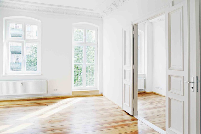 Světlá místnost s dřevěnou podlahou, okny a otevřenými dveřmi