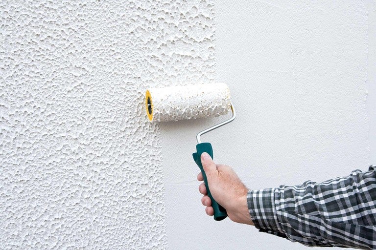 Osoba válí válečkem na barvu po stěně se strukturou omítky