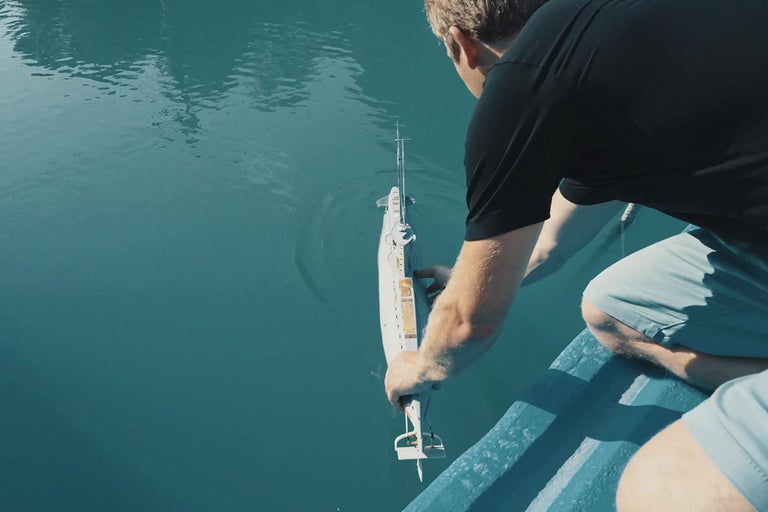 Muž spouští dálkově ovládanou ponorku do vody.