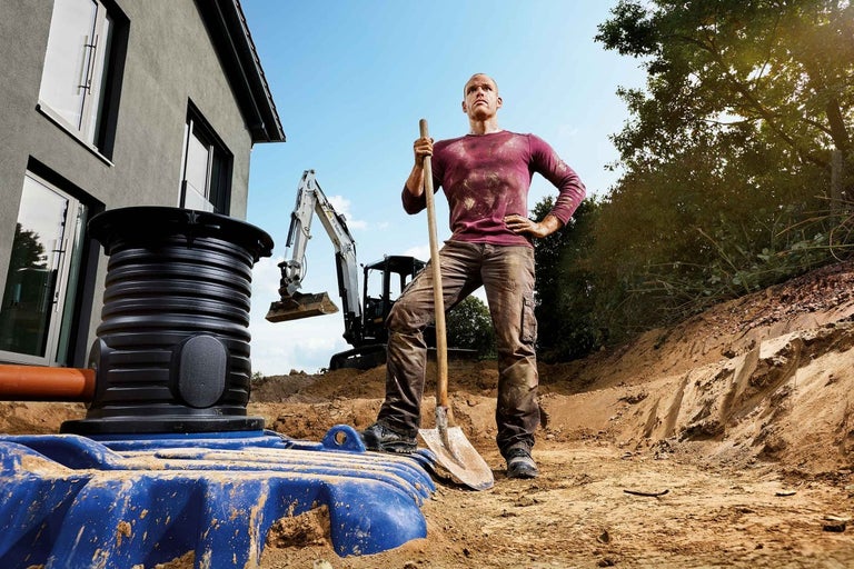 Scéna se septikem, stavebním dělníkem a bagrem na staveništi